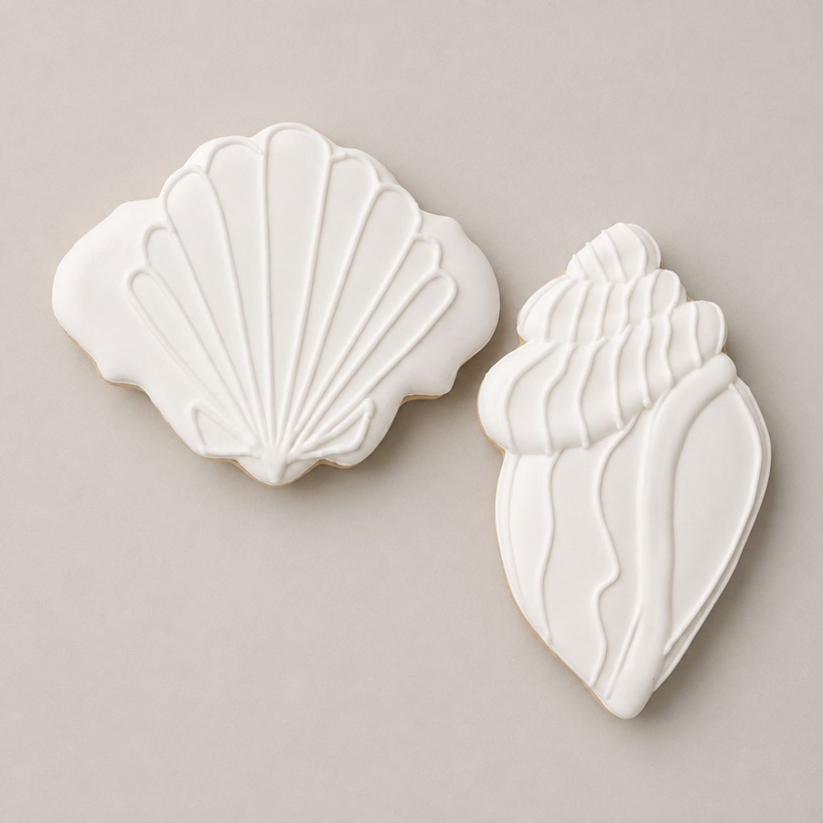 Two cookies iced in white royal icing, a scallop shell and a conch
